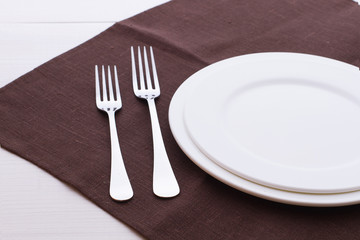 Empty plates, cutlery, tablecloth on white table for dinner.