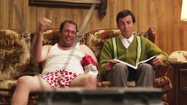 MS TU Obese man wearing underwear sitting on sofa next to geek laughing, watching television, Orem, Utah, USA