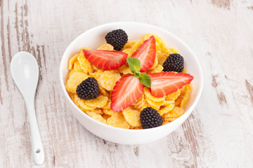 cornflakes with berries in a bowl and milk for breakfast, close-