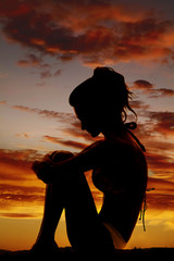 silhouette of a woman in a bikini sit side arms around knees