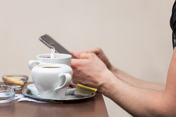 Man texting on his cell phone with a cup of tea on the table