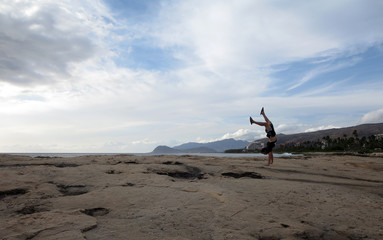 Man wearing a t-shirt, shorts, and slippers Handstands on shore