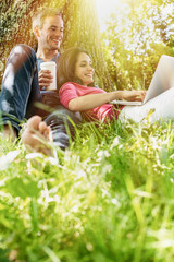 Naklejka na ściany i meble A nice couple sitting in the grass, using a laptop
