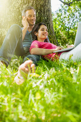 A nice couple sitting in the grass, using a laptop