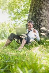 handsome grey hair man using a laptop, barefoot in the grass