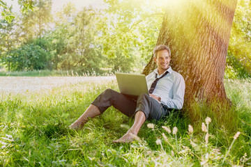 Naklejka na ściany i meble handsome grey hair man using a laptop, barefoot in the grass