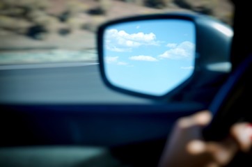 clouds in blue sky in rearview mirror of moving car