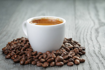 cup of fresh espresso with coffee beans on oak table