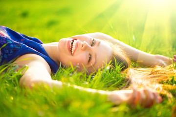 Beautiful young woman lying on the field in green grass