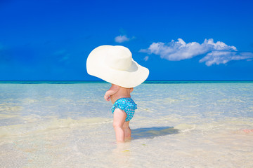 Fototapeta na wymiar A little kid in a large white straw hat having fun on a tropical