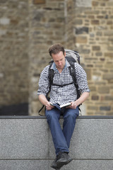 Hiker Reading Book While Sitting On Retaining Wall