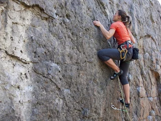 Foto op Plexiglas Jonge vrouw met touw klimt op de rots. © zhukovvvlad