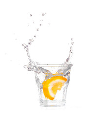 orange splashing into glass of water on white background