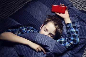 enfant garçon au lit avec smartphone - obrazy, fototapety, plakaty