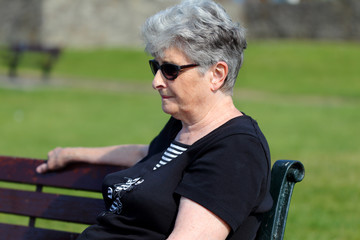 Older lady relaxes outside on a park bench