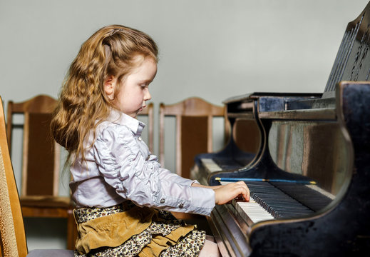 Cute little girl playing grand piano in music school