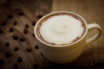 Cup of cappuccino served on wooden table with coffee beans in th
