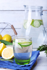 Fresh water with lemon and cucumber in glassware on napkin on wooden table, closeup