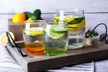 Fresh water with lemon and cucumber in glassware in wooden tray, closeup