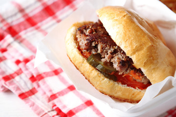 Tasty burger on paper napkin, on wooden table background, close-up. Unhealthy food concept