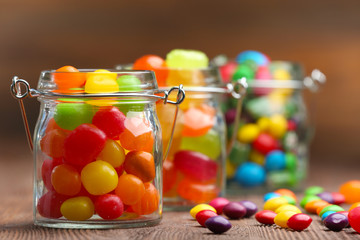 Colorful candies in jars on table on wooden background