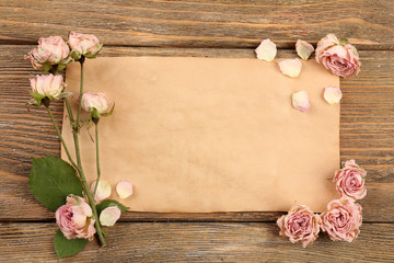 Dried roses on sheet of paper on wooden table, top view