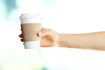 Female hand with paper cup on bright blurred background