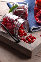 Red currant in glass jars on wooden tray, closeup