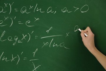 Female hand writing formulas on blackboard with chalk, close up