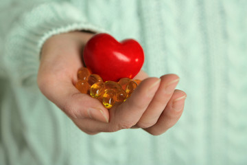 Hand holding red heart and cod liver oil, close up