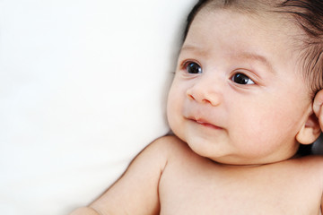 Cute baby is looking up to someone on white bed