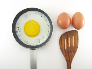 fried egg in pan, two raw eggs and spatula isolated on white background