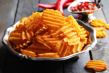 Delicious potato chips on plate on wooden table close-up