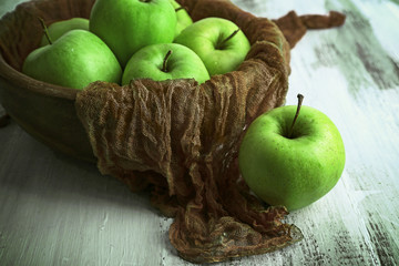 Green apples in bowl with fabric on wooden table, closeup