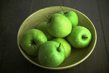 Green apples in bowl on wooden table, closeup