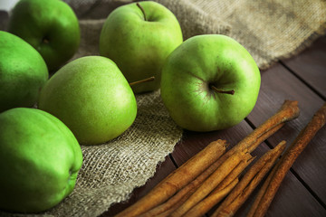 Green apples with cinnamon sticks on wooden table with sackcloth, closeup