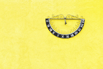 Sun dial clock on a yellow wall