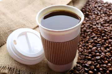 Paper cup of coffee with beans on sackcloth close up