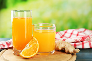 Glass of orange juice and slices on wooden table, on bright background