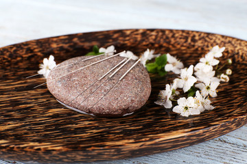 Acupuncture needles on wooden plate with pebble and flowering branch, closeup
