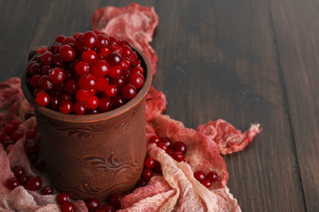 Red cranberries in clay cup on wooden table with scarf, closeup