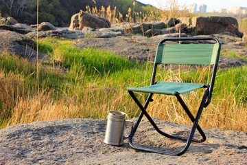 Camp chair and thermos cup on nature background