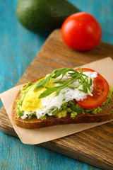 Tasty sandwich with egg, avocado and vegetables on cutting board, on color wooden background