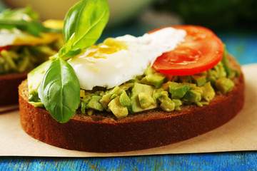 Tasty sandwich with egg, avocado and vegetables on paper napkin, on color wooden background