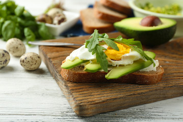 Tasty sandwich with egg, avocado and arugula on wooden background