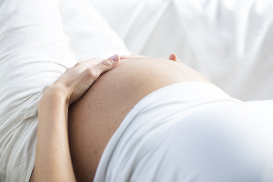 Schwangere Frau hält Hände schützend um Bauch, Detail