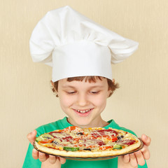 Little smiling boy in chefs hat with a cooked homemade pizza