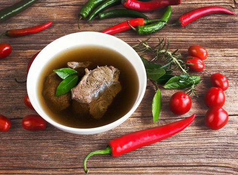 Beef broth with meat with vegetables on wooden background