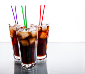 three glasses of cola with ice and straws on a white background.