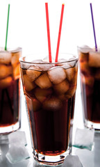 three glasses of cola with ice and straws on a white background.